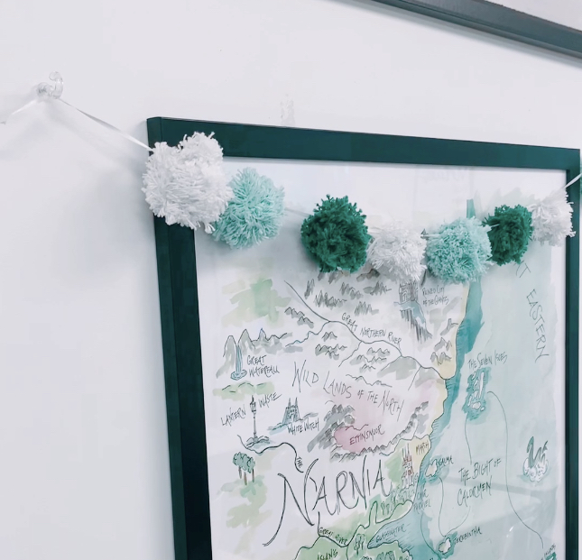 pin hooks holding up a pom-pom banner over a map of Narnia in the classroom